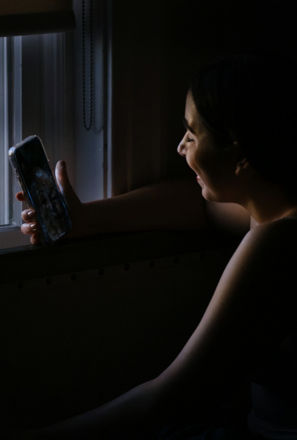 A person smiles while looking at their smartphone indoors.